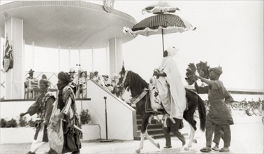 Durbar for Queen Elizabeth II, Nigeria. A Nigerian chief sits beneath a ceremonial umbrella as he