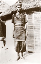 A Nigerian policeman at Minna. A uniformed Nigerian policeman stands outside a thatched village