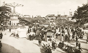 Fairground at British Empire Exhibition. Bustling crowds explore the fairground rides and stalls at