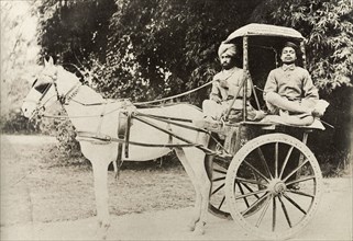 A horse-drawn tonga. An Indian driver and his passenger sit cross-legged on a horse-drawn tonga.