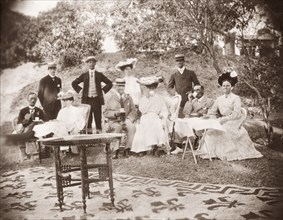 A Victorian picnic. A group of Victorian men and women drink cups of tea whilst picnicking in the