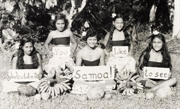Wouldn't you like to see Samoa'. Five young Samoan women sit cross-legged on the grass, holding up