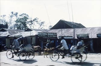 Cycle rickshaw drivers in Dibrugarh. Cycle rickshaw drivers whizz past shops with tin roofs on a