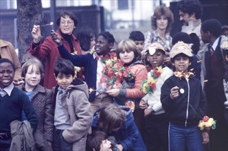 Children light sparklers at an outdoor carnival. A group of schoolchildren wearing masks and floral