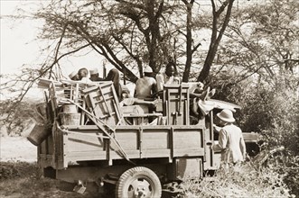 Jeep made ready for safari. African porters sit amongst a jumble of folding tables and chairs in