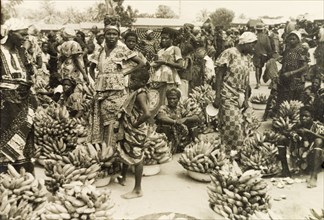 Banana stalls at a busy marketplace. Female traders sell hands of bananas from bowls at a bustling