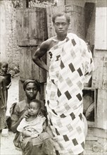 An Asante family. An Asante (Ashanti) man stands beside his seated wife and baby, wearing a