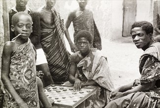 Asante boys playing a board game. A group of Asante (Ashanti) youths gather round to watch two boys