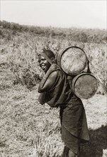Kikuyu woman carrying water. A Kikuyu woman carries water in two barrels on her back, supported by
