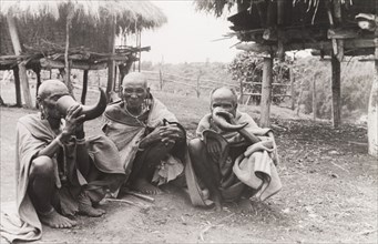 Kikuyu elders drinking beer. Three Kikuyu elders squat on the ground as they drink beer from hollow