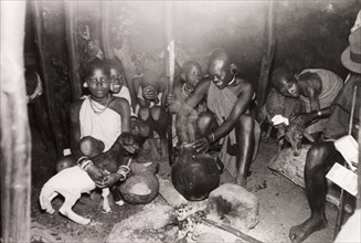 Evening meal in a Kikuyu hut. A Kikuyu woman serves an evening meal to her family, who are gathered