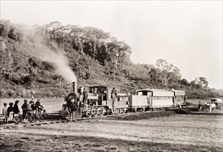 A steam train at Limuru. African railway staff gather around a stationary steam train on a track at