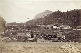A Ceylon Government Railway track. Two men sit beside an empty rail cart on tracks belonging to the