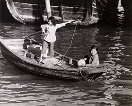 Chinese girls steer a sampan. Two girls travel aboard a scull-propelled sampan in Aberdeen Harbour,