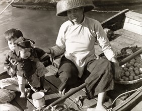 Selling fruit from a sampan. A woman with two young children sells fruit from a sampan in Aberdeen