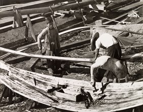 Constructing a sampan. Two men build a sampan at a boatyard in Aberdeen Harbour, whilst a third
