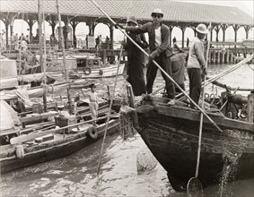 Fishing in a Hong Kong harbour. Fishermen stand at the bow of their sampan, dipping long-handled
