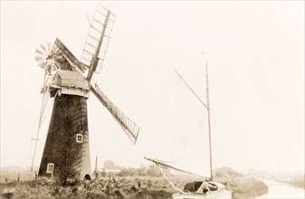 Sailing on the Norfolk Broads. A boat sails past a windmill as it travels along a river on the