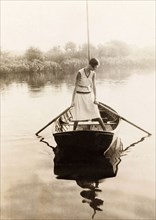 Rowing on the Norfolk Broads. A lady stands alone in a rowing boat on a river in the Norfolk Broads