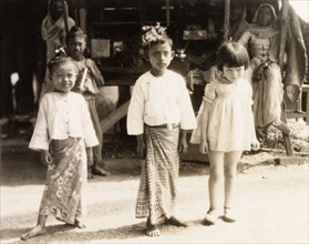 Children in Rangoon. A young British girl poses with two Burmese children wearing traditional
