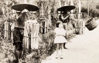 Transporting firewood, Kuala Lumpur. A young British girl visiting Kuala Lumpur stands between two