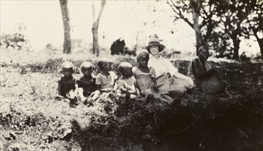 European woman with Chaga children. A European woman sits on a grassy bank with a Chaga woman and