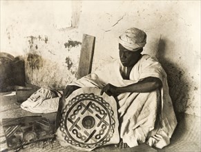 A Nigerian leatherworker. A Nigerian leatherworker sits in his workshop, holding up a decorative