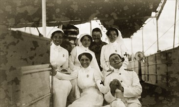British officers with Indian nurses. Two British military officers pose on the deck of a ship with