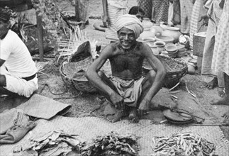 Street trader in Ceylon. A street trader sells a variety of dried foods at a busy outdoor market.