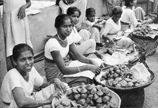 Short-eats' in Ceylon. A row of female traders sit on a city street, selling deep-fried