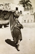 Palestinian woman collecting water. A Palestinian woman in traditional Arabic dress balances a clay