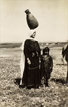 Bedouin woman carrying water pot. A bedouin woman stands with a young child in the Palestinian