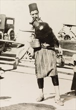 Cold drink seller, Palestine. A street peddler with a large jug strapped to his chest stands by the