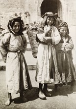 Child basket carriers, Palestine. Three Palestinian children pose on a city street, each carrying a