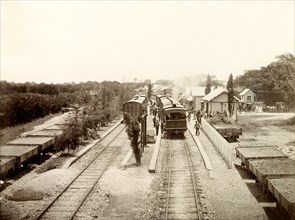 San Joseph railway station, Trinidad. Flatbed freight cars loaded with gravel sit beside passenger