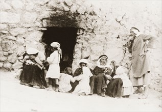 An Arab family, Palestine. An Arab family sit at the entrance of a stone dwelling. British Mandate