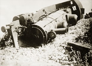 Derailed steam locomotive at Ras el Ain. A steam locomotive lies upturned on a railway embankment,