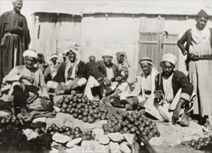 Oranges for sale, Palestine. Several Arab men sit on the ground, surrounded by heaps of oranges for
