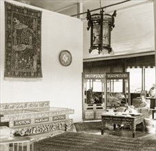 Asian artefacts in a colonial drawing room, British Malaya. Dr Reid Tweedie sits reading in the