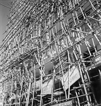 Bamboo scaffolding with adverts, Calcutta. A tall building is encased in bamboo scaffolding as it