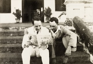 Reading 'Punch' magazine. Mr Moulton and Mr Horler sit on the steps of the United Theological