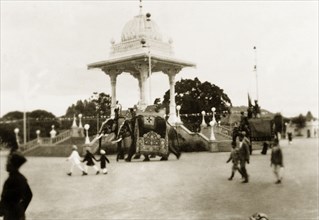 Elephant procession at Dasara Festival. Caparisoned elephants parade past a monument in Mysore