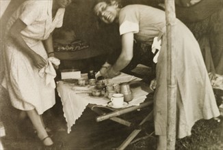 Nurses at a missionary medical camp. Two European nurses prepare drinks in a tent at a Methodist