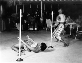 Limbo dancing at the Anchorage Hotel. A female limbo dancer passes beneath a horizontal pole