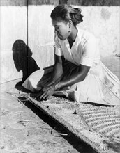 Weaving a palm mat, Dominica. A young woman sits on the ground as she weaves a mat from palm fibre.