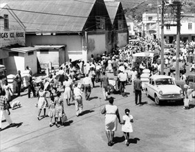 Market day in Kingston, St Vincent. Crowds of people and traffic fill a side street in Kingstown on