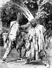 Carnival dancers on Nevis. Two men perform a carnival dance outdoors. Both wear crowns adorned with