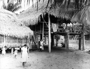 An Amerindian village in British Guiana. Amerindian women and children relax outdoors below the
