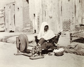 Silk spinner, India. An Indian woman sits by the roadside spinning silk using a 'charkha' or