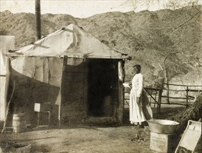 Living quarters at Red Cloud Mine. An African woman wearing an apron stands at the doorway of a